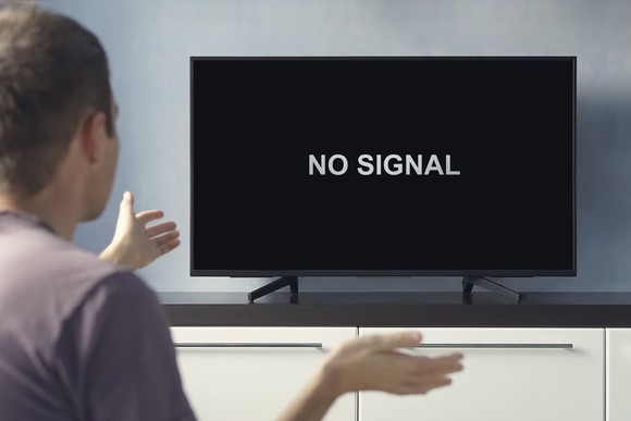Person staring at black TV screen with white words saying No Signal. 
