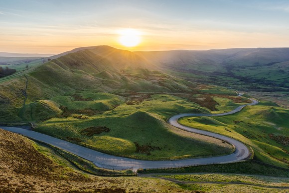 A winding road through a lush valley at sunset. 