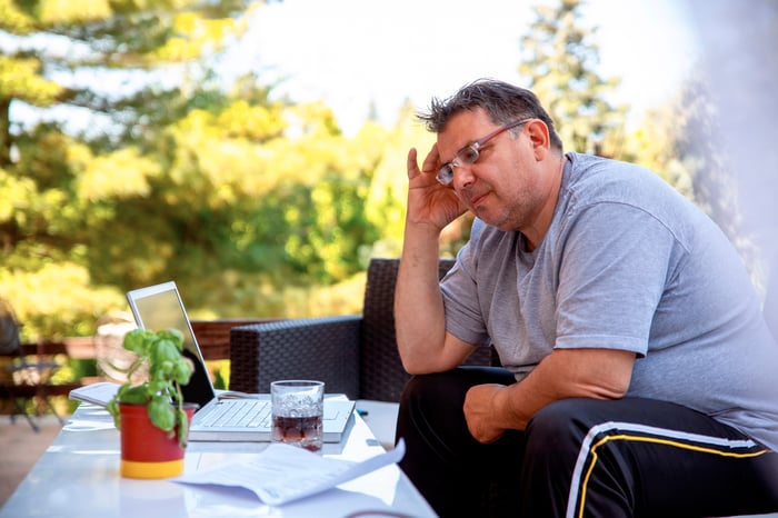 Someone is sitting outdoors with a laptop, hand on his head, looking very regretful.