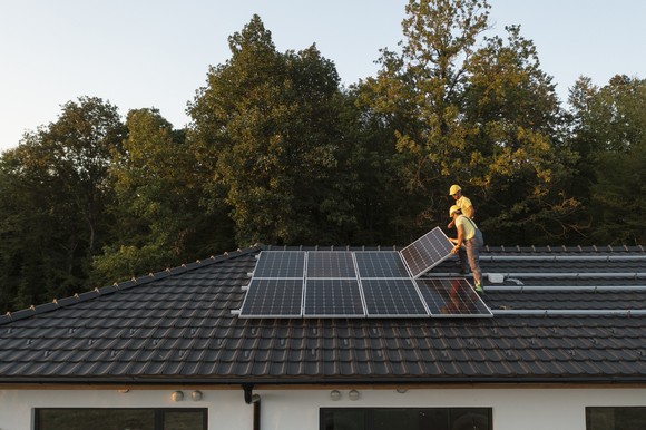 Technicians install solar panels on house. 