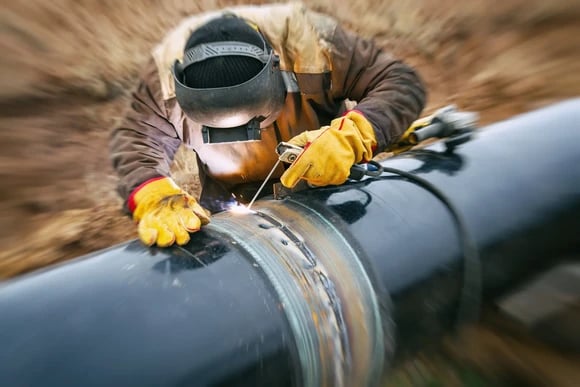 A close up of a welder working on a pipeline.