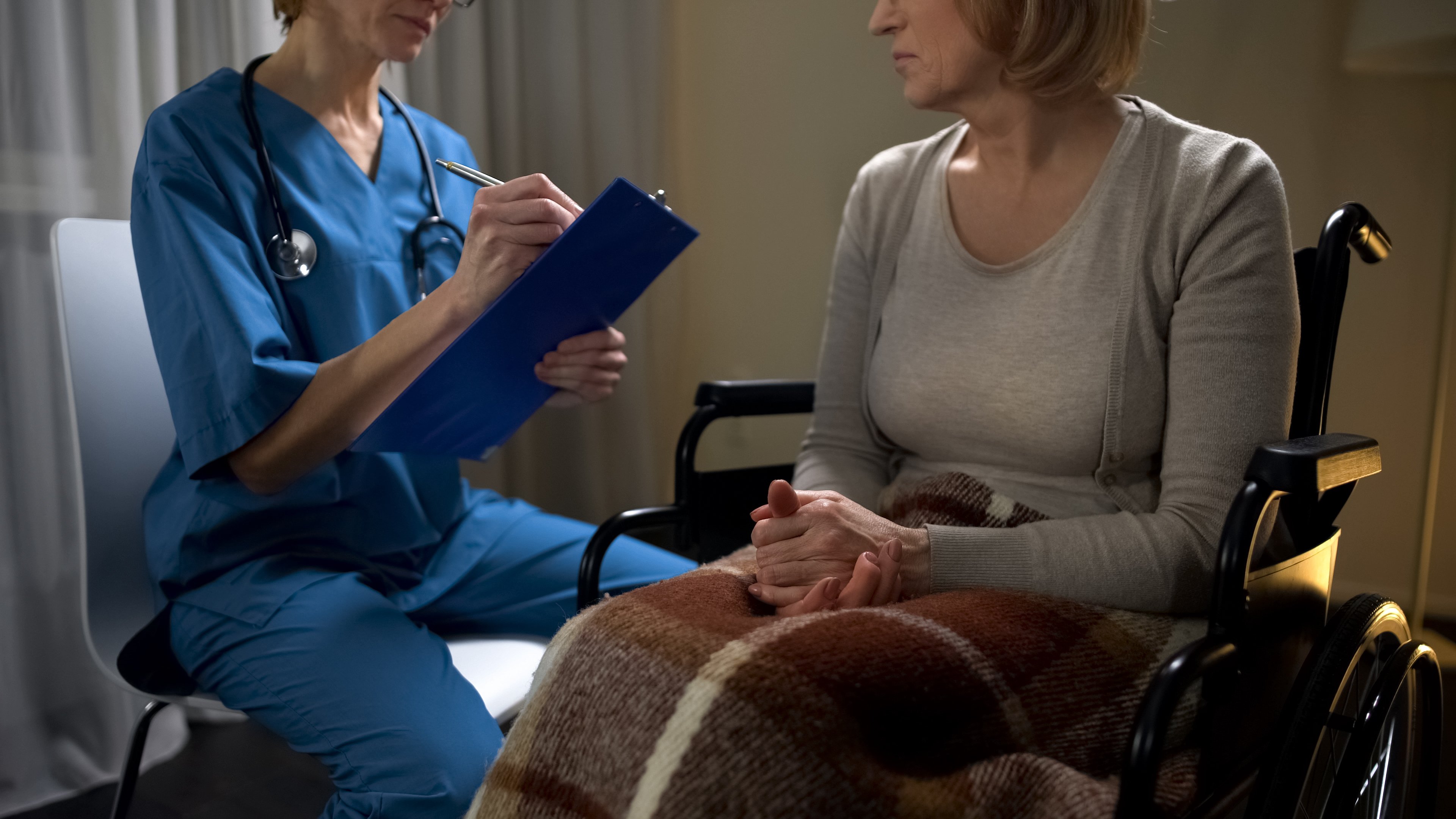 A doctor, a clipboard, and a patient using a wheelchair.