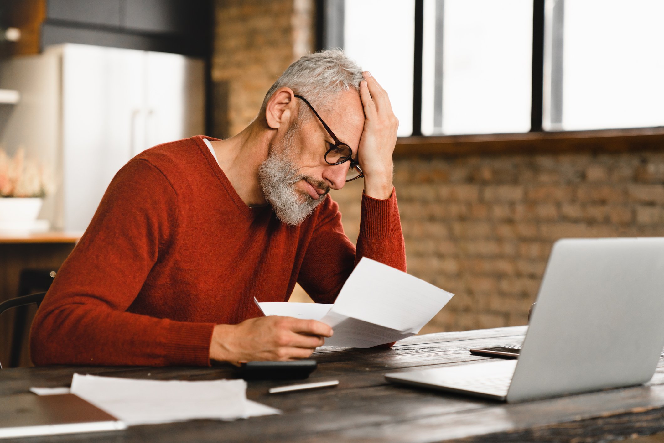Older man stressed holding document at laptop