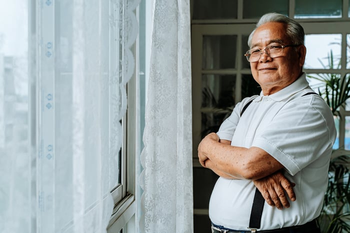 Someone in suspenders is standing near a window, looking at the camera.