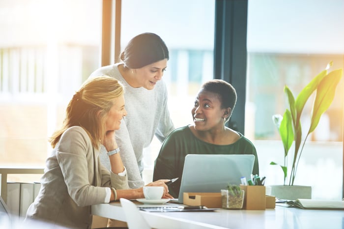 Three people gather around a laptop and collaborate.