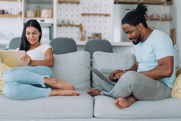 Two people sitting on a couch while looking at their laptops.