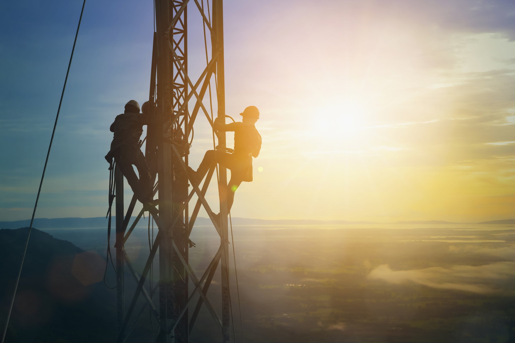 Silhouettes of electricians working high above ground.