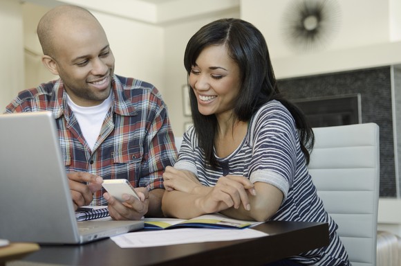 Two people smiling while working together on a laptop computer.