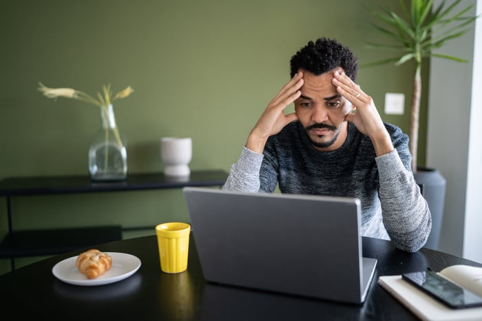 A person at a laptop holding their head.