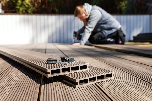 A carpenter using a drill to place composite boards on a deck.