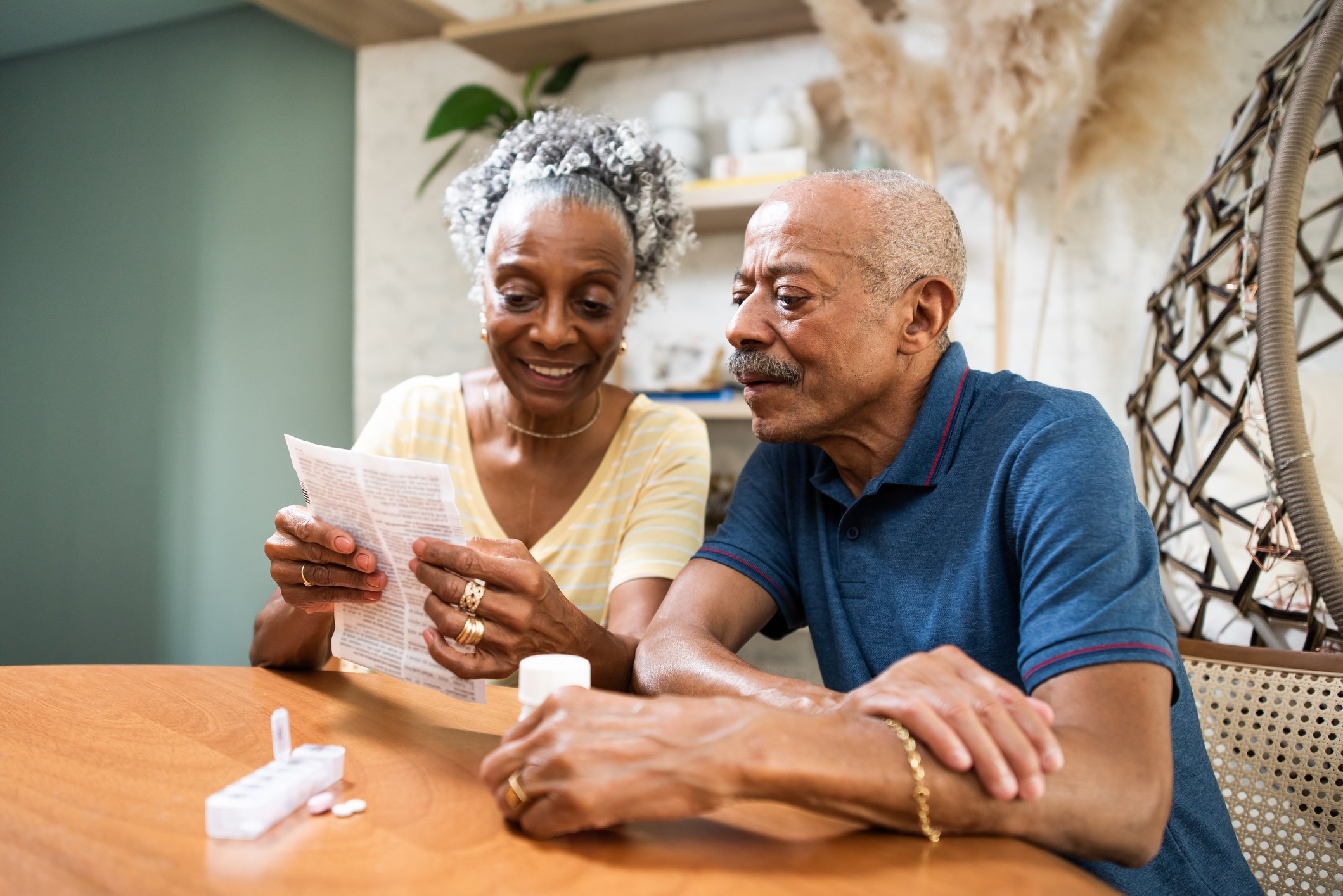 Two people looking at a document with a pill bottle and pills on the table in front of them.