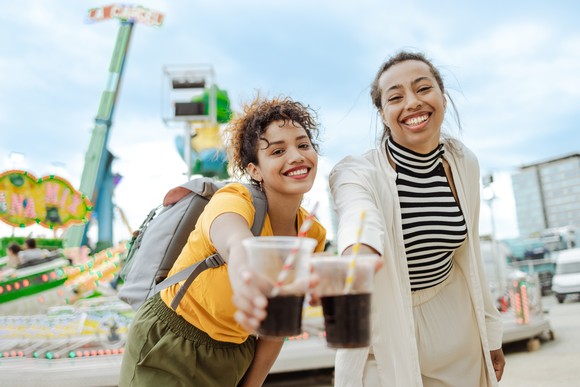 Two smiling people holding out cups of soda.