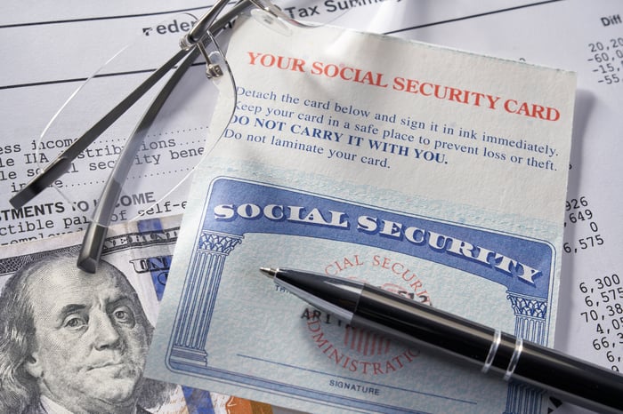 A Social Security card sitting atop a $100 bill and a financial document.