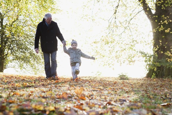 An adult and child walk through leaves outside.