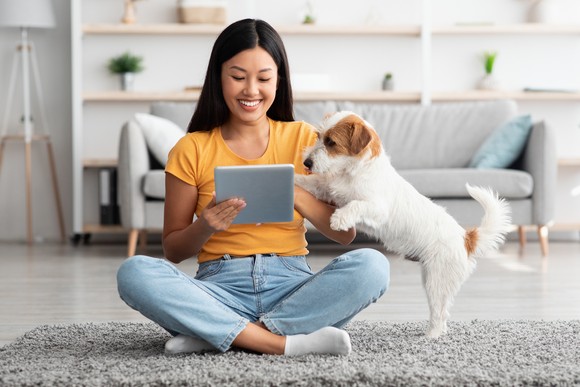 A person sits on the floor and looks at a tablet with a dog.