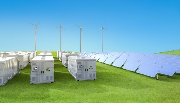 A rural site with energy storage systems, panels, and wind turbines.