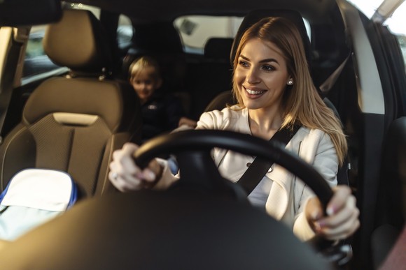 Person driving car with child in backseat.