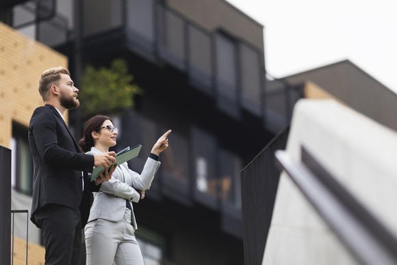 Two professionals stand outside while reviewing a property.