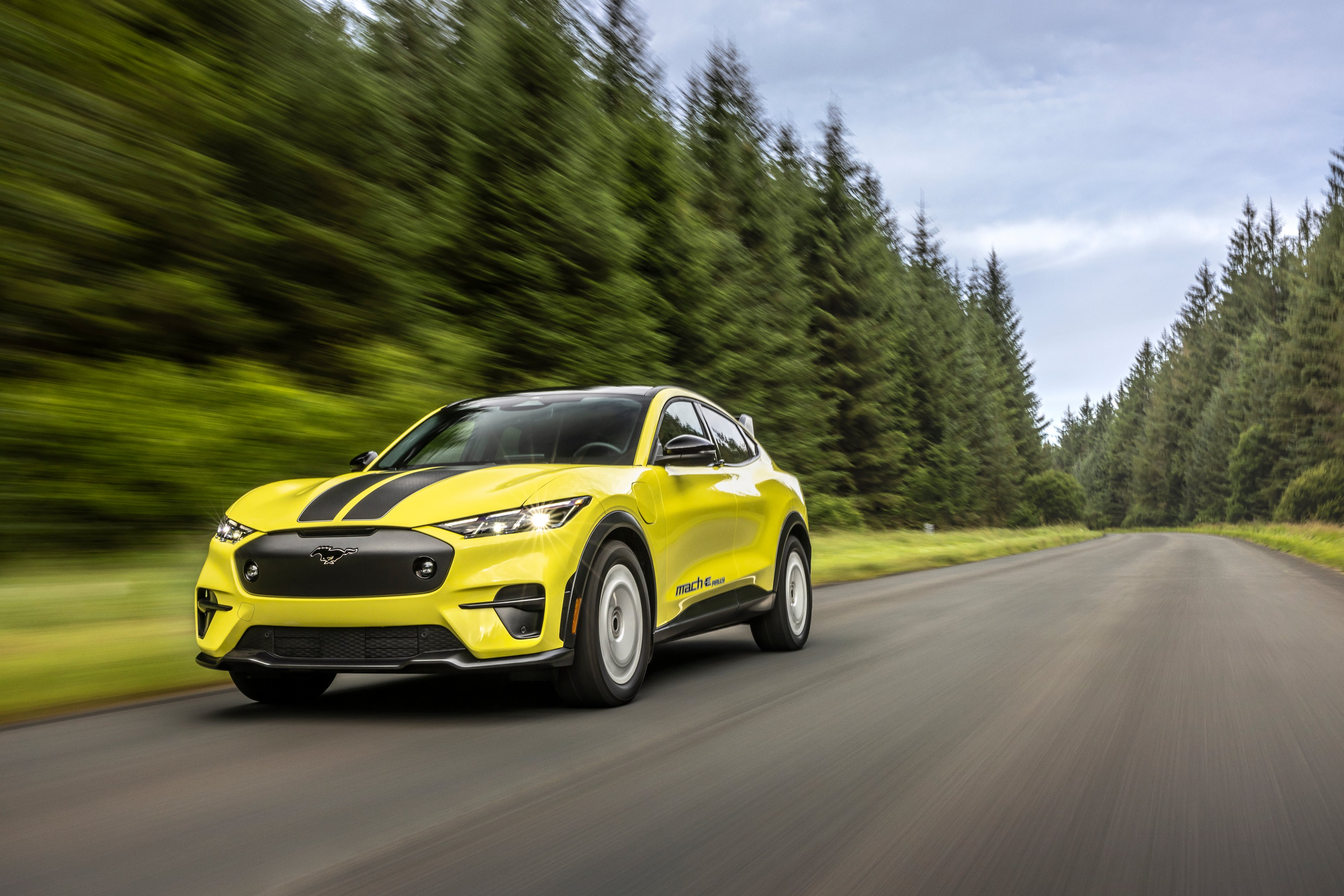 yellow Mustang Mach E racing down forested road.