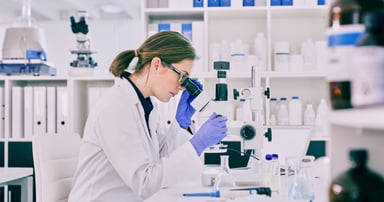 scientist peers in microscope in lab