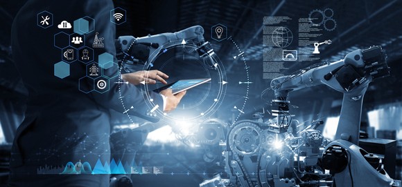 An artist rendering of the overlap between robotics and human interaction as seen through a person holding a tablet surrounded by several icons, charts, and machinery.