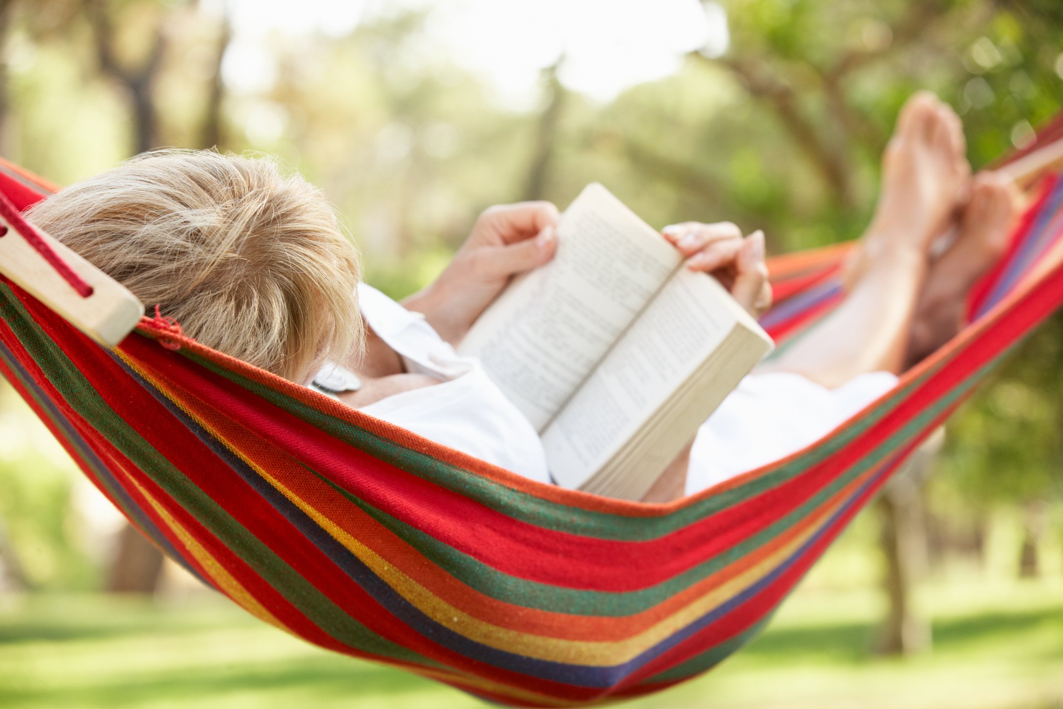 Person shown from the back, lying in a hammock, reading a book.