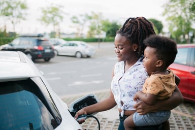 A person with a baby charging an electric car.