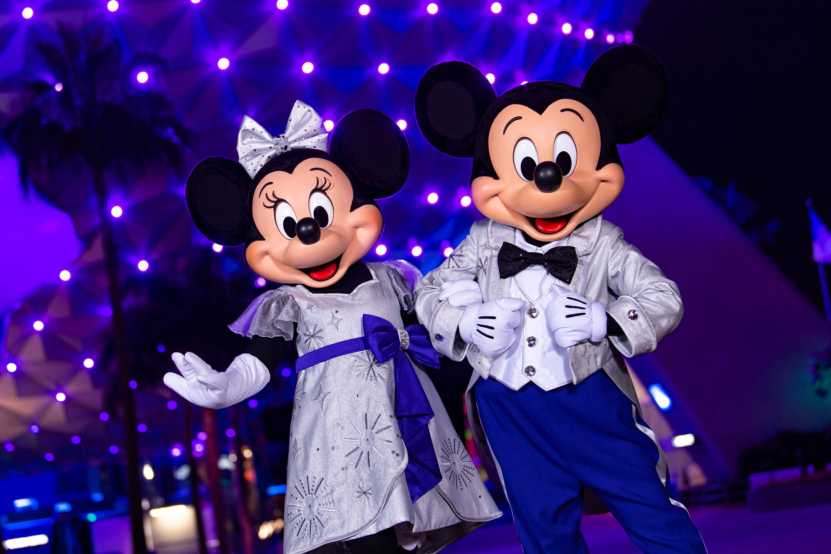 Mickey and Minnie posing in front of Epcot's Spaceship Earth at night.
