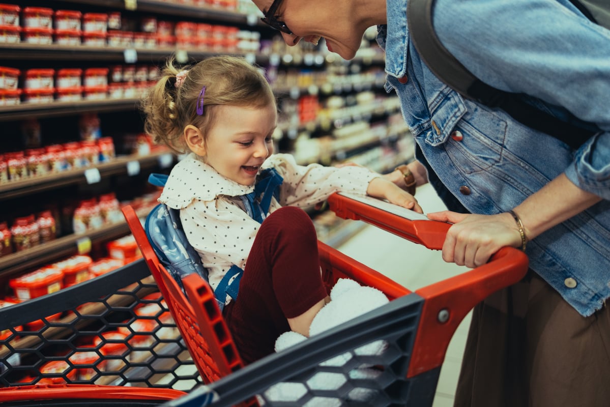 A child smiles while being pushed in a red  shopping cart.