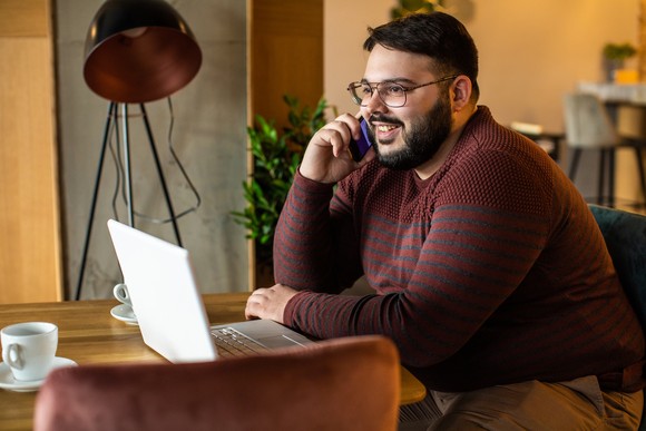 An investor in a home office smiles while talking on the phone.