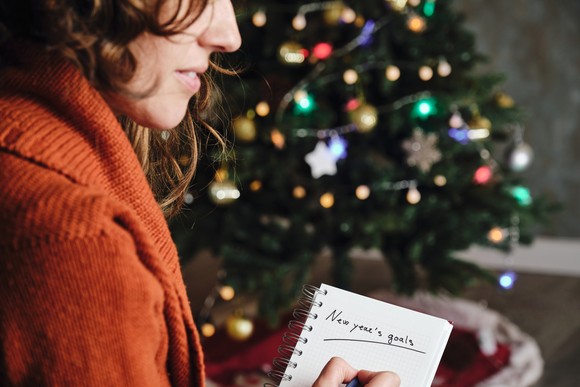 An investor writes something in a notebook while sitting near a Christmas tree.