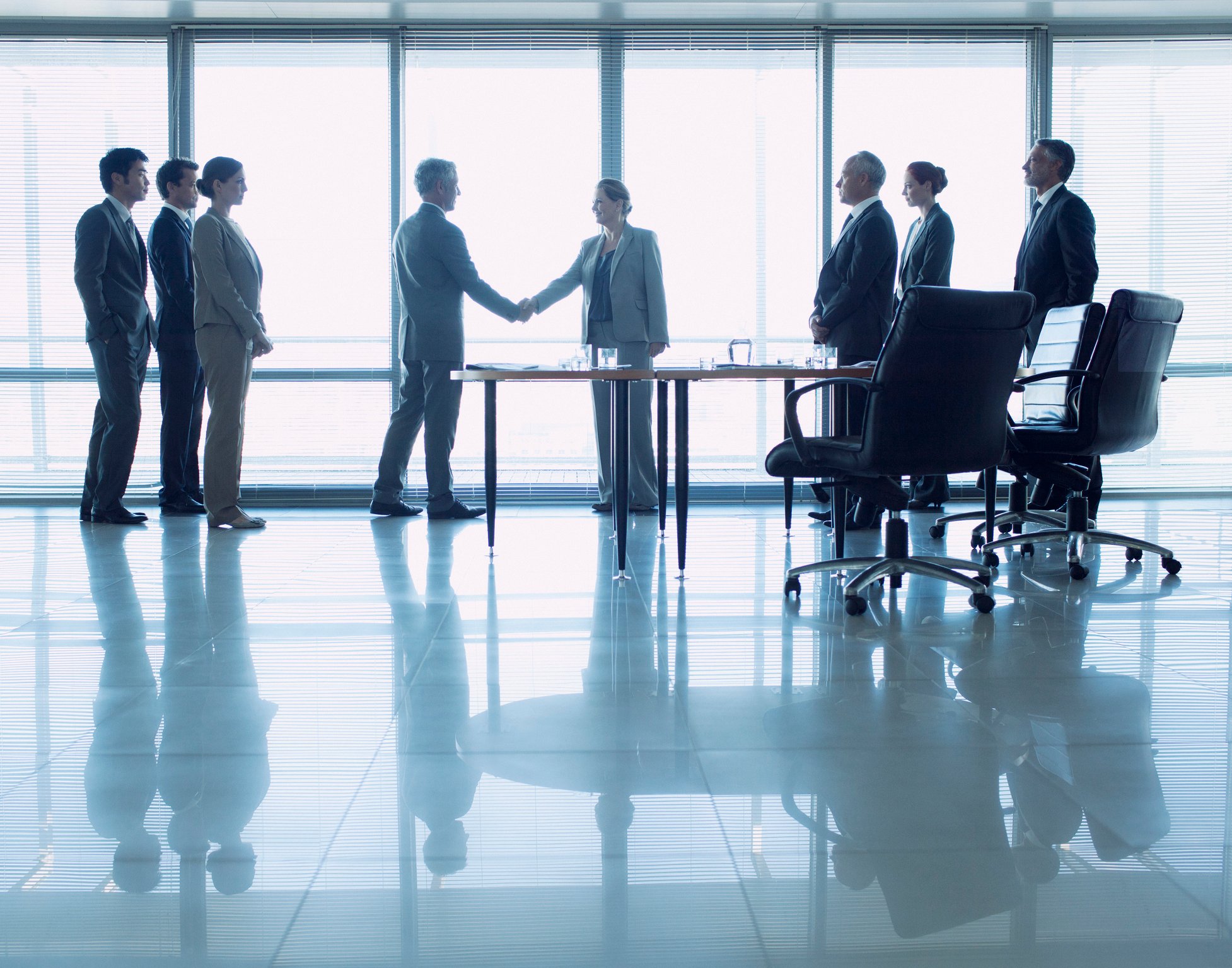 Group of professionals in a conference room, with two people shaking hands.