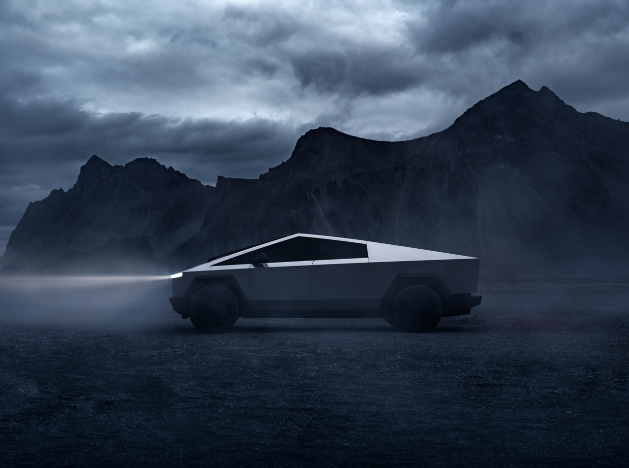 An all-electric Tesla Cybertruck with its lights on driving through a mountainous area during cloudy weather.
