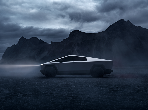 An all-electric Tesla Cybertruck with its lights on driving through a mountainous area during cloudy weather.