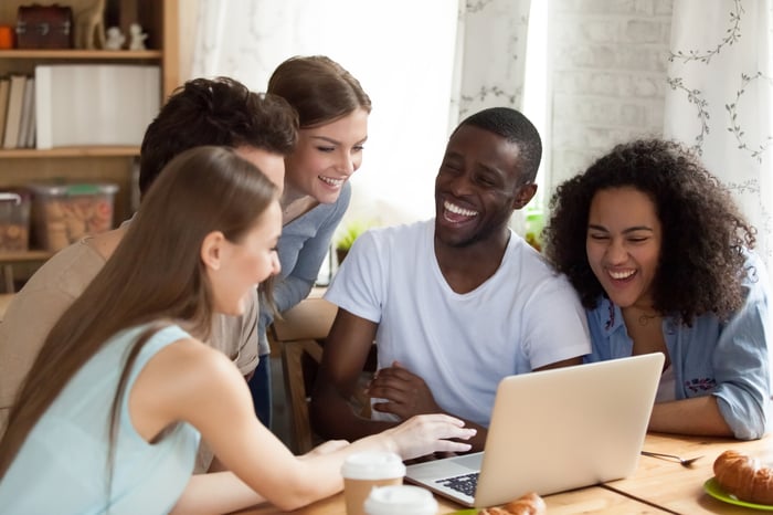 A group of investors smile as they crowd around a laptop.