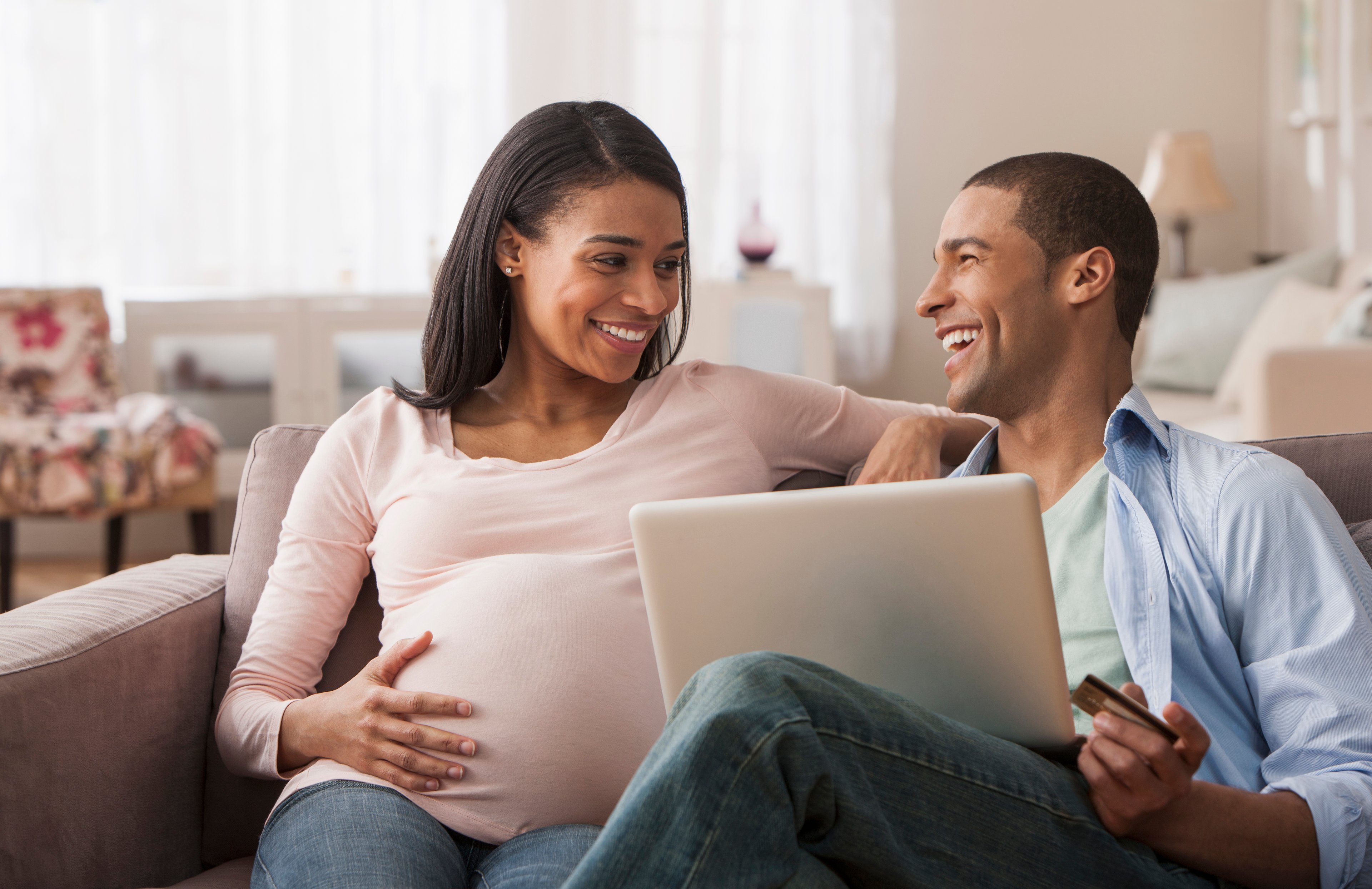 A smiling couple sitting together on a couch using a laptop.