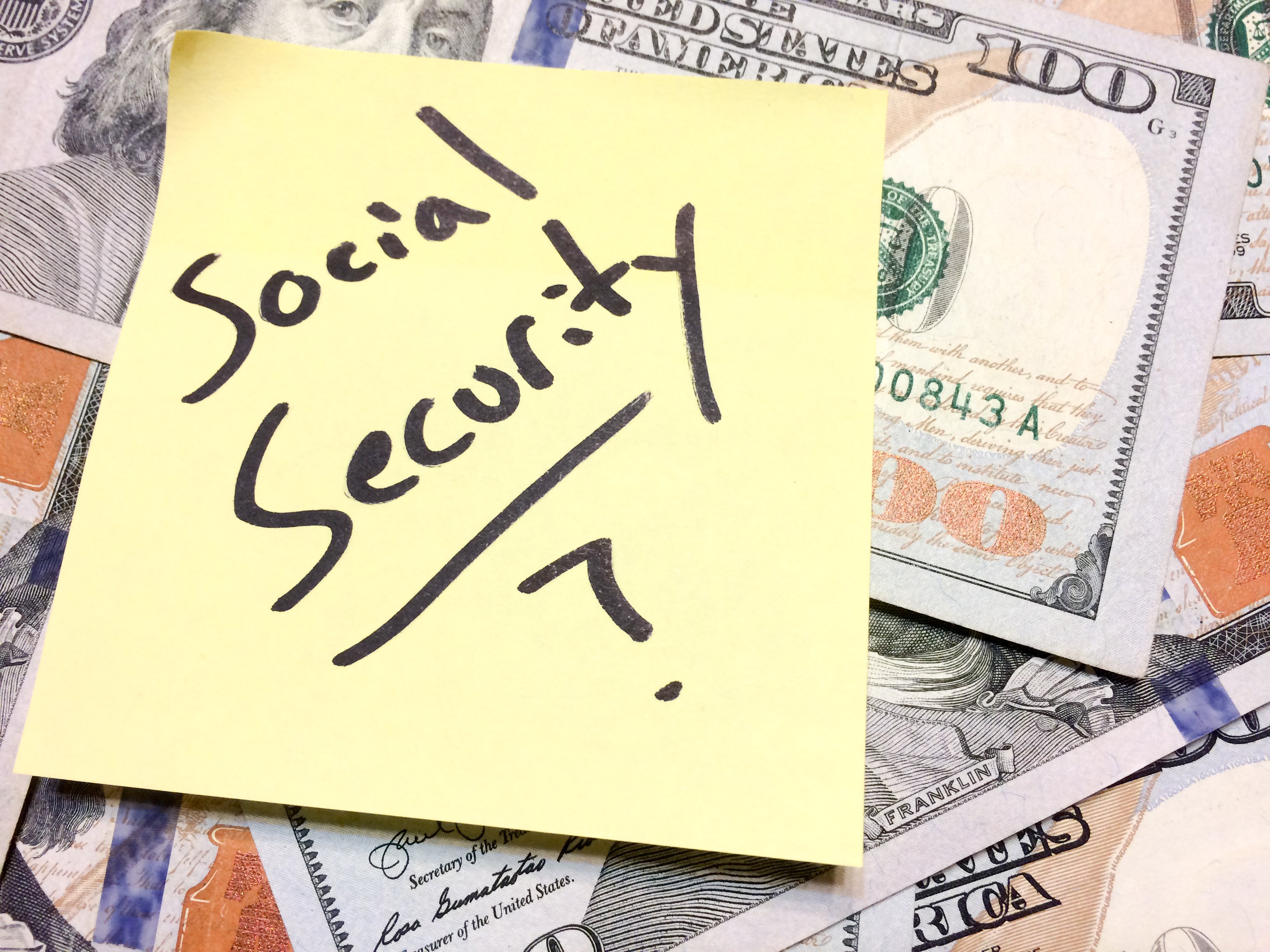 A post-it note reading "Social Security?" sitting atop a pile of cash.