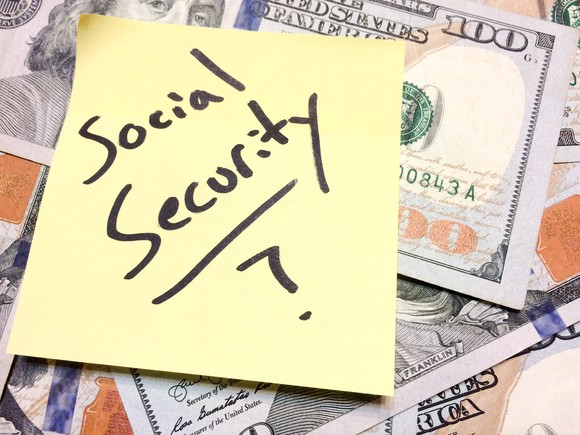 A post-it note reading "Social Security?" sitting atop a pile of cash.