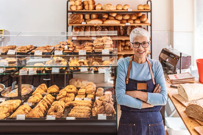 A person in an apron standing in front of a bakery display.