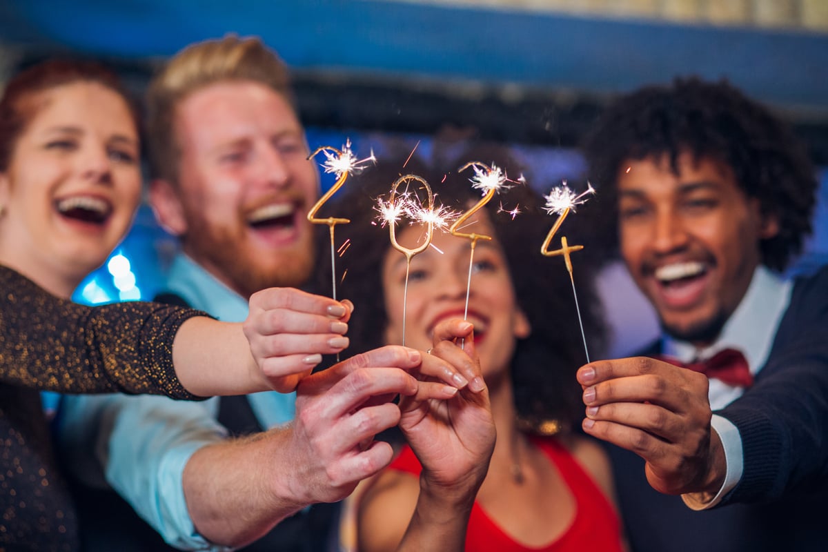 Four people smile and hold up sparklers showing "2024."