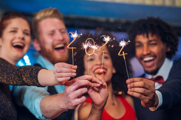 Four people smile and hold up sparklers showing "2024."