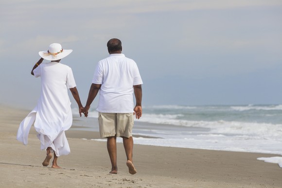 Two people walking down a beach holding hands.