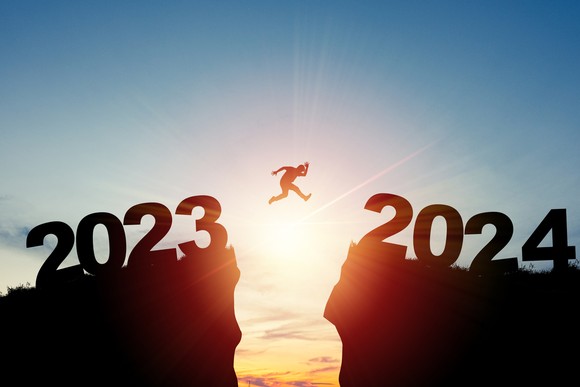 A person jumping from one cliff that reads "2023" to another that says "2024."