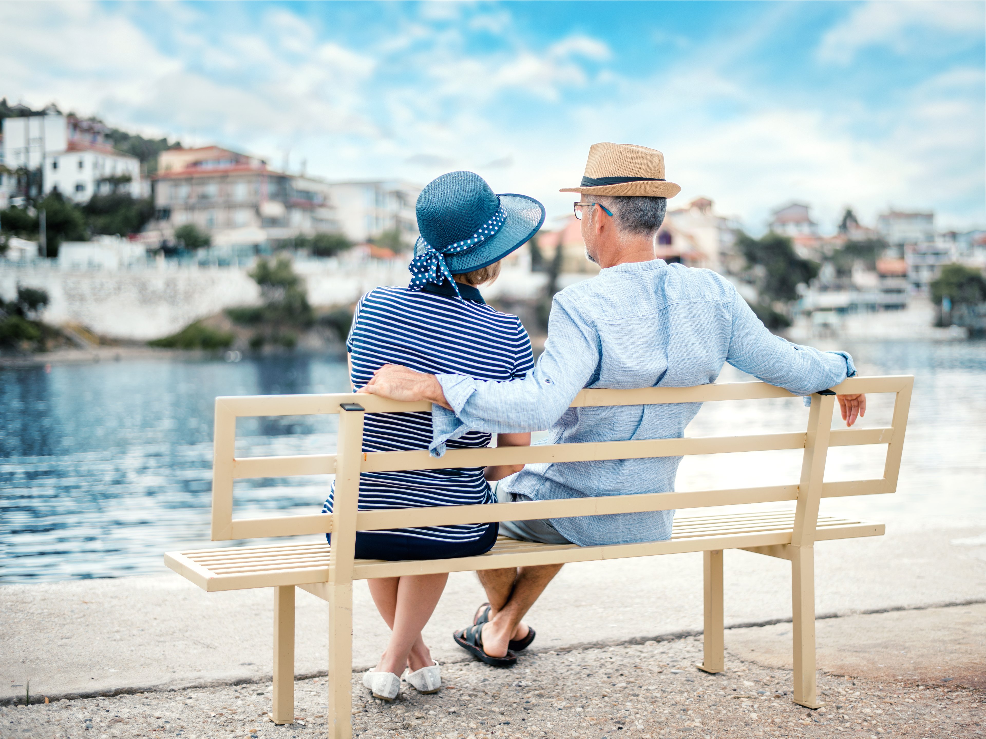 Two people relaxing on a bench next to the water, looking at a hillside town.