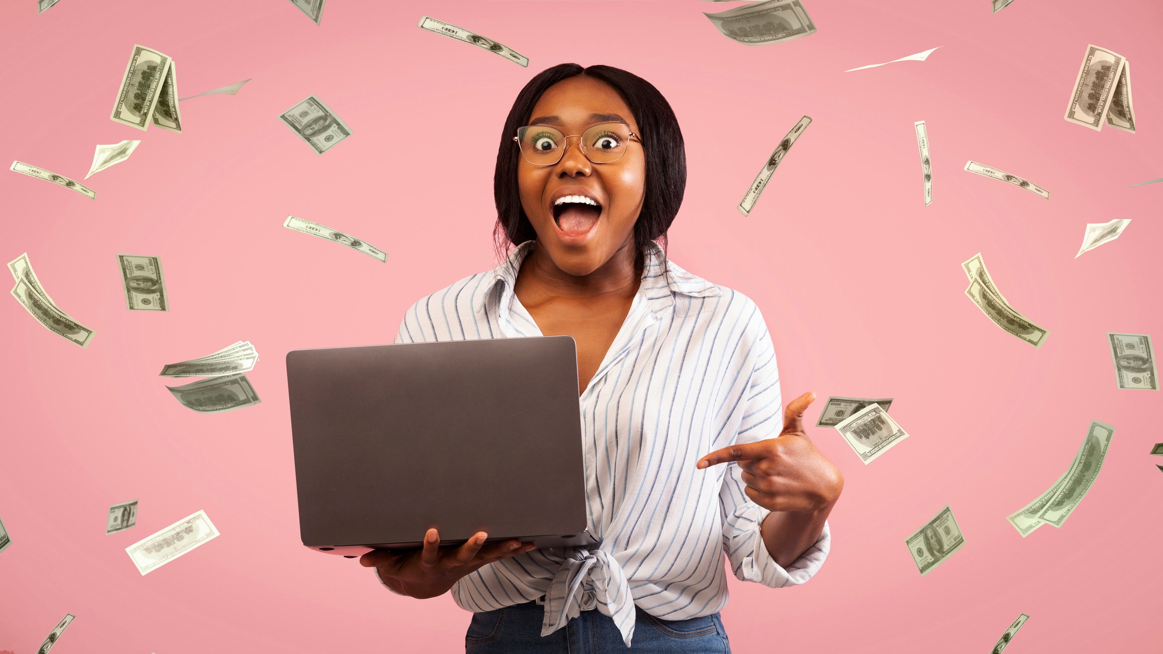 A happy person is showered with cash while checking a laptop.