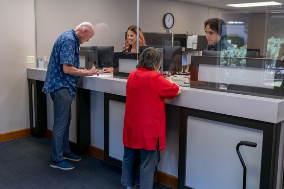 Two customers standing at the desk of a bank interacting with bank employees.