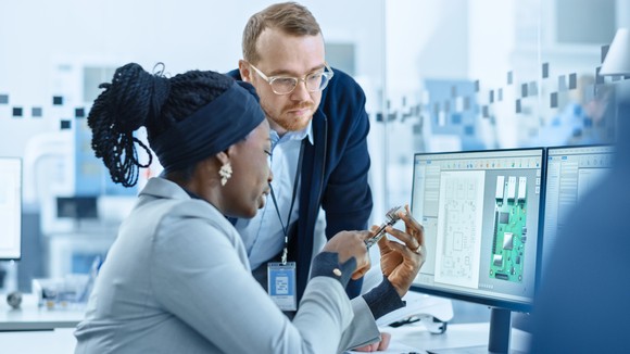 Two people inspecting a circuit board. 