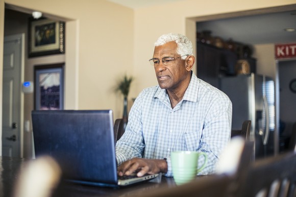 Someone sitting at a table typing on a laptop.