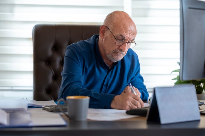 A person seated at a desk holding a writing instrument.