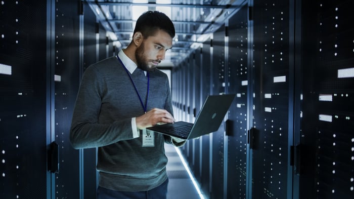 Person with laptop standing in corridor of servers.